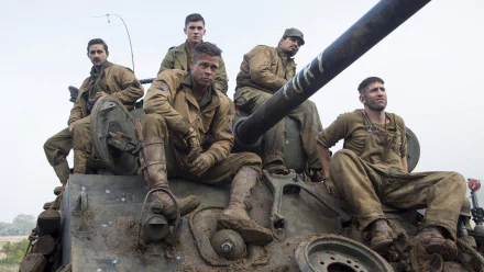 A gripping scene from the movie Fury, featuring Shia LaBeouf, Brad Pitt, Logan Lerman, Jon Bernthal, and Michael Peña, captured atop a tank in muddy military attire.