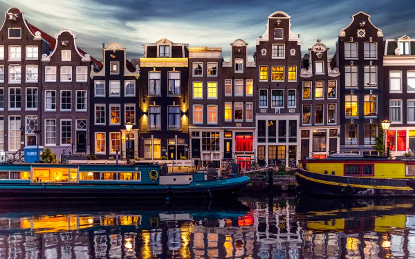 A vibrant Amsterdam canal scene featuring colorful houseboats reflecting in the water, framed by historic, beautifully lit buildings that embody the charm of the city.