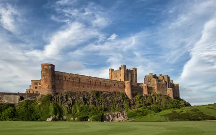 Bamburgh Castle, a man-made medieval fortress on a grassy Scottish headland beneath a dramatic blue sky — HD PC desktop wallpaper and background.