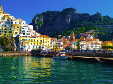 HD desktop wallpaper showcasing a vibrant Amalfi Coast village with colorful houses, boats docked by the ocean, and mountains towering in the background.