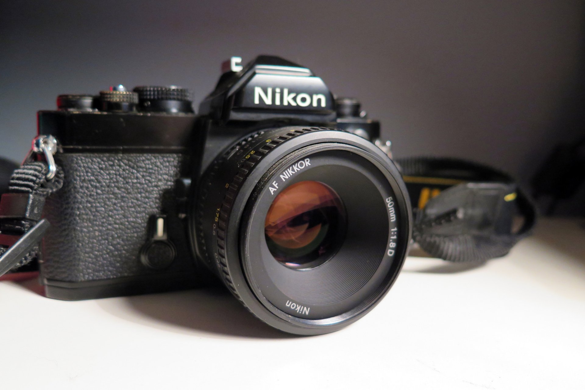 Close-up of a Nikon camera with prominent lens on a neutral surface — HD PC desktop wallpaper background featuring a man-made camera in sharp detail.
