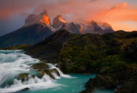 A stunning sunset illuminates the dramatic peaks of the Torres del Paine in Patagonia, as a cascading waterfall flows through a lush landscape, capturing the beauty of nature.