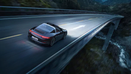 Black Porsche 911 Targa driving across a mountain bridge at dusk — 2K Quad HD PC desktop wallpaper of the Porsche 911 sports car in motion.