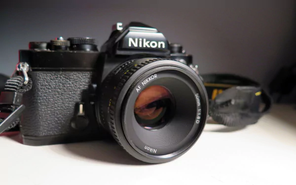 Close-up of a Nikon camera with prominent lens on a neutral surface — HD PC desktop wallpaper background featuring a man-made camera in sharp detail.