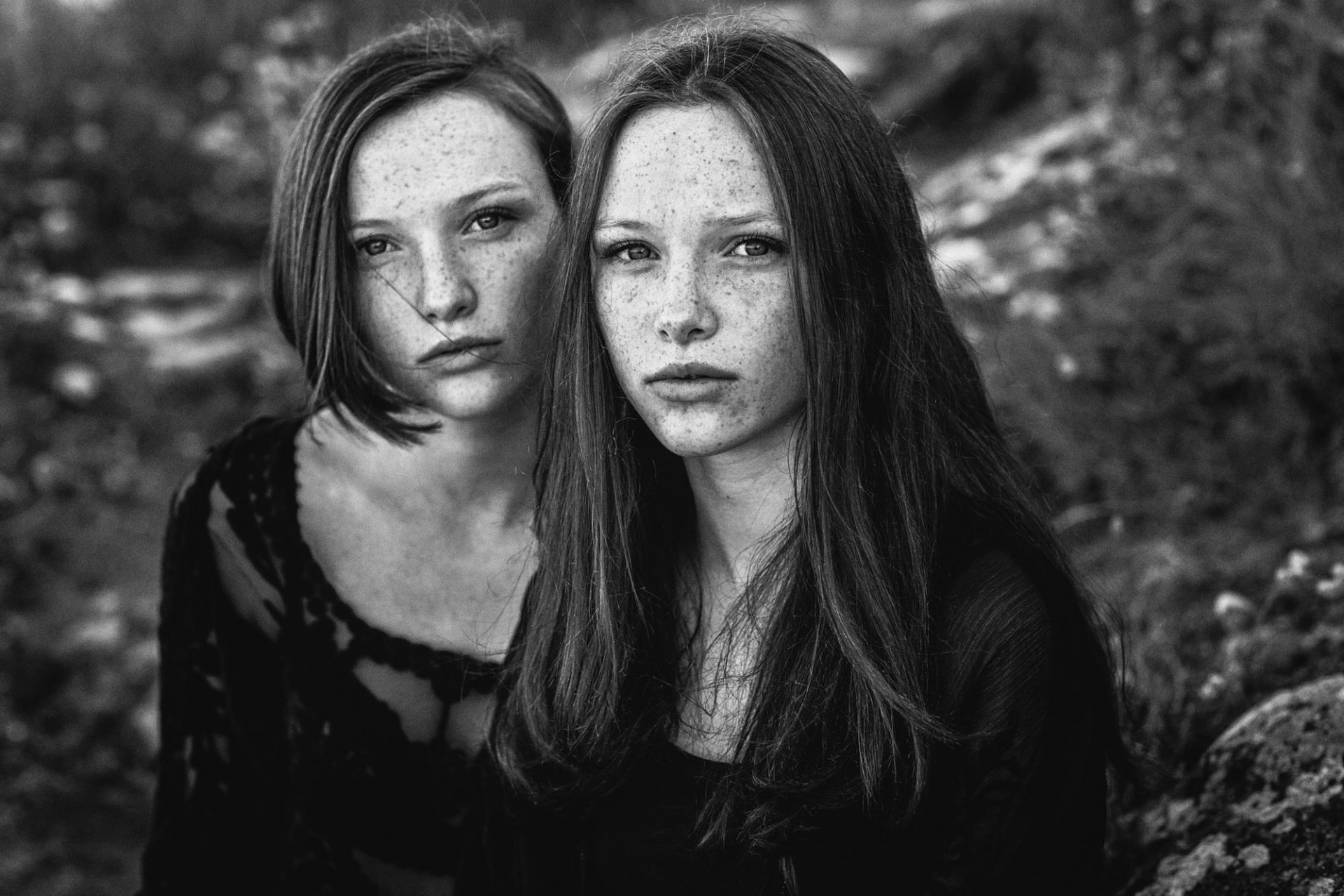 Black and white HD desktop wallpaper featuring two freckled women with serious expressions, captured in a natural outdoor setting.