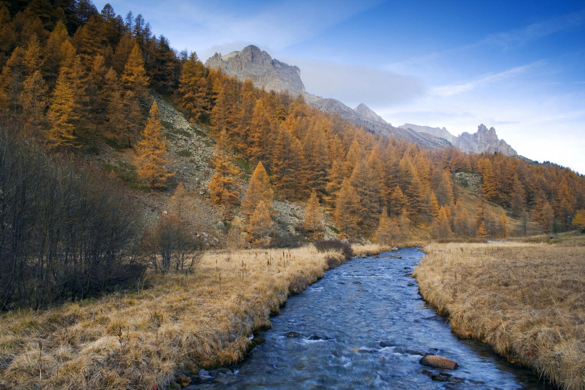 HD PC desktop wallpaper showcasing a serene river flowing through a golden autumn forest with distant mountain peaks under a clear blue sky.