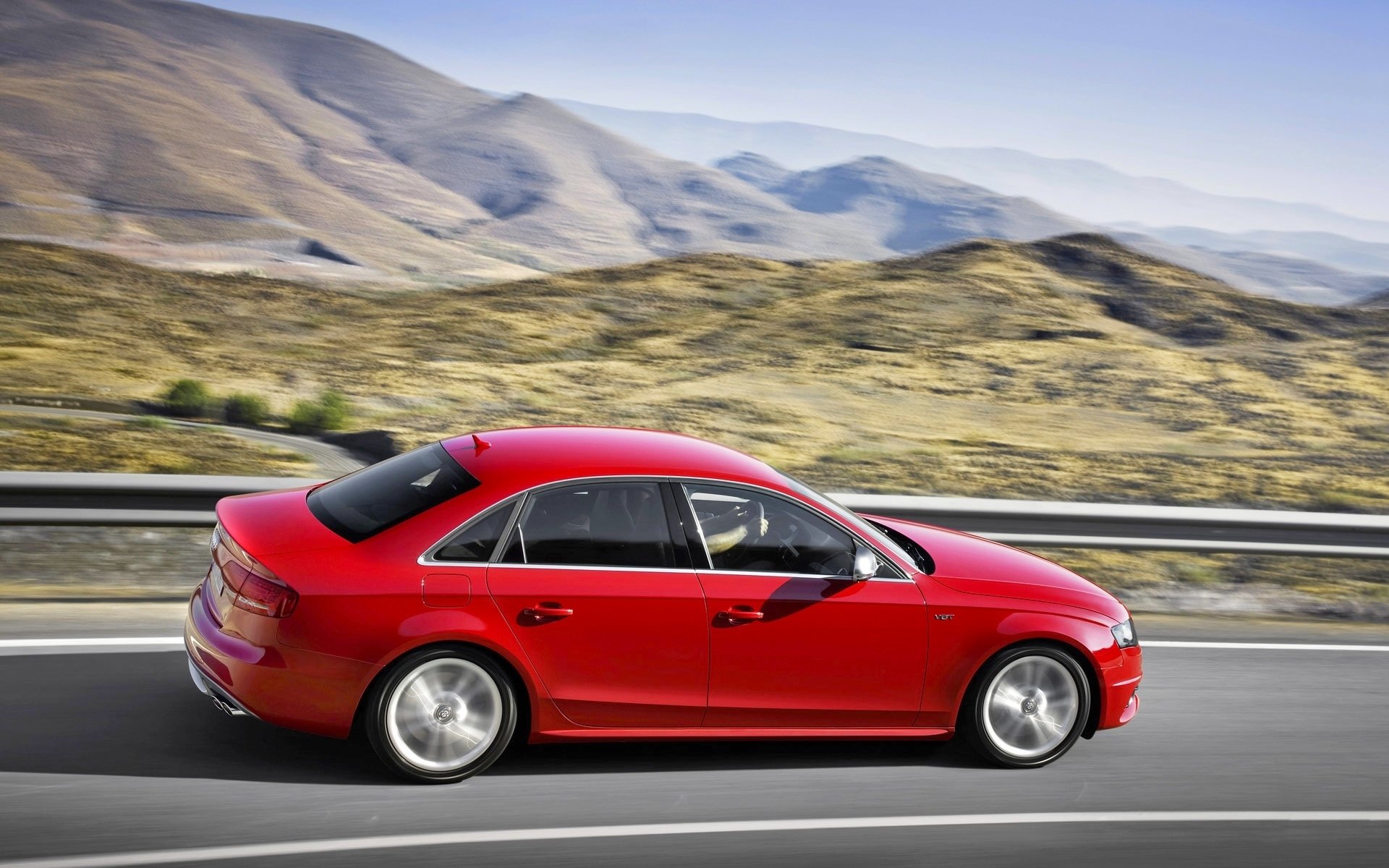 HD desktop wallpaper featuring a red Audi S4 car driving on a highway with mountains in the background, showcasing the vehicle's sleek design and dynamic presence.