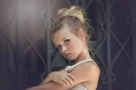 A blonde little girl poses thoughtfully against an ornate background. This captivating photograph is a stunning 4K Ultra HD wallpaper, showcasing the innocence of childhood.