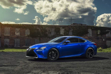 HD desktop wallpaper featuring a blue Lexus RC car parked in front of an old brick building under a partly cloudy sky.
