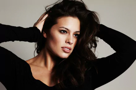 HD PC desktop wallpaper featuring American model Ashley Graham with brown eyes and brunette hair posing with hands in her hair against a neutral background.