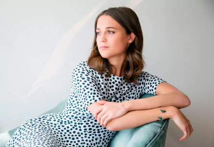 Alicia Vikander, Swedish actress with brunette hair and brown eyes, posed thoughtfully against a light background in this HD PC desktop wallpaper.