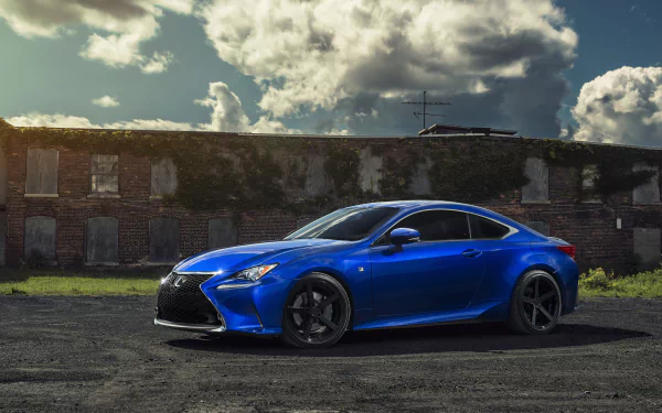 HD desktop wallpaper featuring a blue Lexus RC car parked in front of an old brick building under a partly cloudy sky.