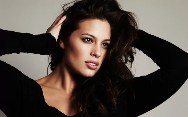 HD PC desktop wallpaper featuring American model Ashley Graham with brown eyes and brunette hair posing with hands in her hair against a neutral background.