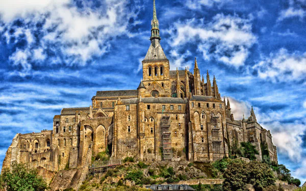 A stunning view of Mont Saint-Michel, featuring its medieval architecture and religious significance, against a dramatic sky. A captivating wallpaper showcasing France's rich history.