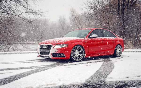 Red Audi S4 parked on a snowy road during winter snowfall, surrounded by bare trees, captured in a high-definition PC desktop wallpaper image.