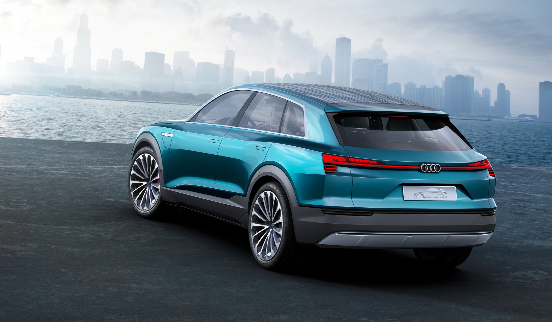 Turquoise Audi E-tron Quattro SUV rear three-quarter view on a waterfront with a misty city skyline, rendered as a 4K Ultra HD PC desktop wallpaper background.