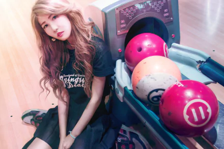 An Asian brunette woman with brown eyes poses beside a bowling ball return machine, featuring colorful balls, in a vibrant HD desktop wallpaper setting.