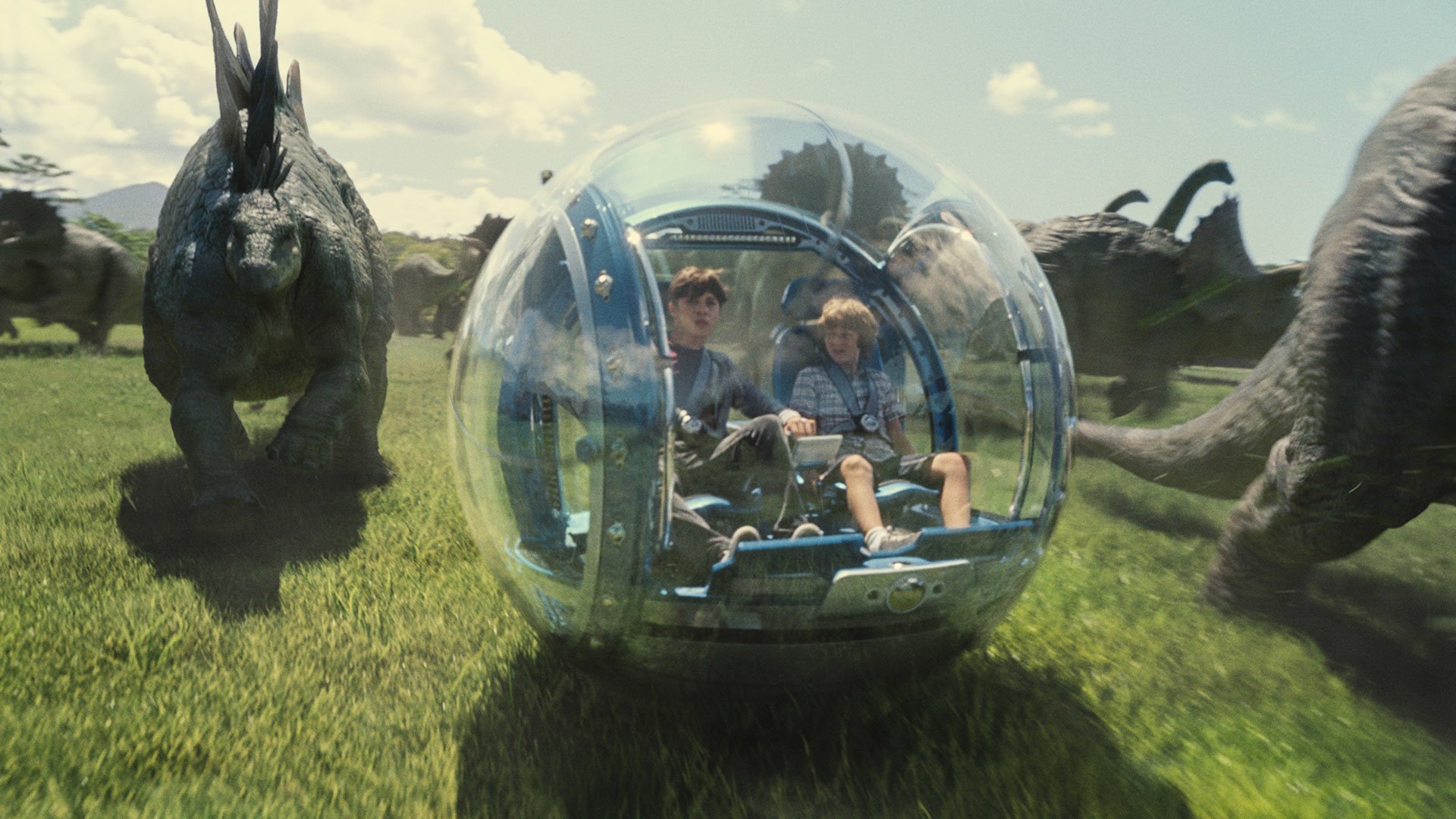 HD PC desktop wallpaper from the movie Jurassic World featuring two characters inside a transparent spherical vehicle surrounded by dinosaurs in a grassy landscape.