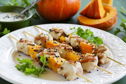 Grilled meat and pumpkin skewers served on a white plate with fresh herbs, set against a backdrop of sliced pumpkin and a bowl of dipping sauce, captured in 4K Ultra HD.