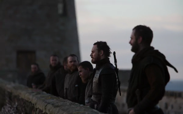 Line of armored men on a stone wall at dusk, central male actor in profile—dramatic Macbeth movie scene; 5K Ultra HD PC desktop wallpaper/background.