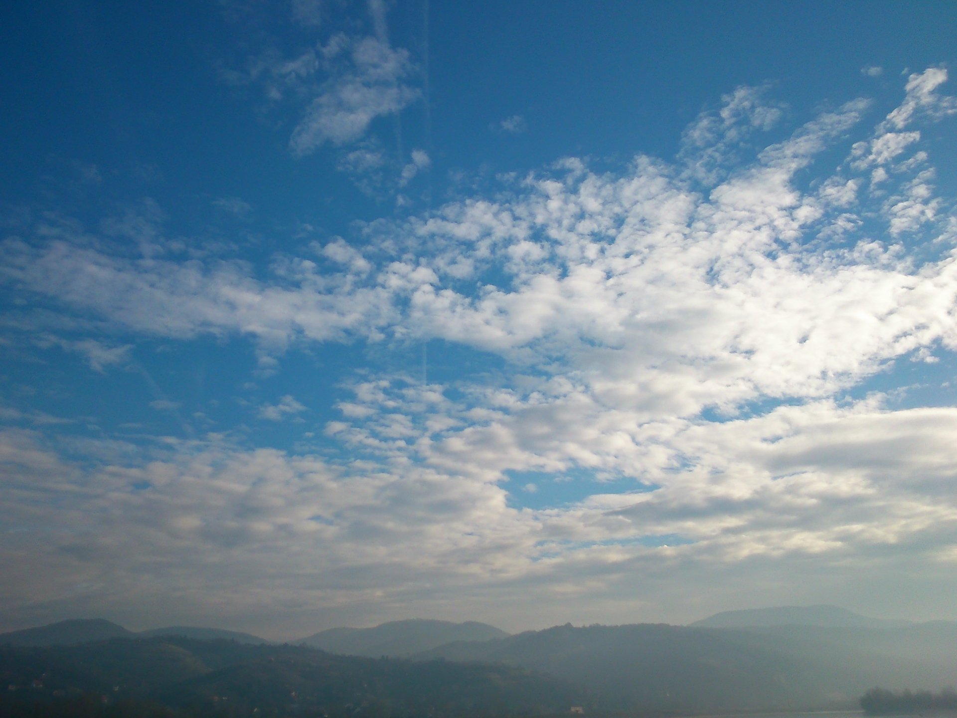 2K Quad HD PC desktop wallpaper: expansive mountain range beneath a sweeping blue sky dotted with wispy clouds, serene nature scene.