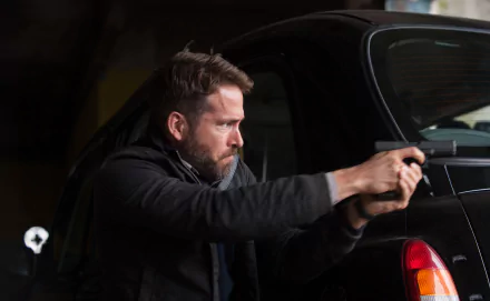 Bearded man aiming a handgun beside a black car in a moody night scene, cinematic still from the movie Criminal (2016), 4K Ultra HD PC desktop wallpaper.