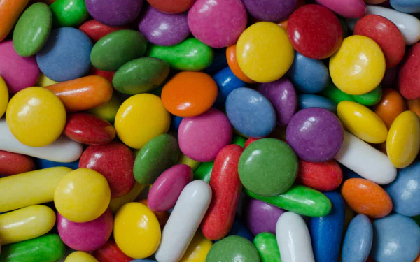 A vibrant assortment of Smarties candies in various colors sprawls across the image, creating a colorful and inviting backdrop for any desktop wallpaper.