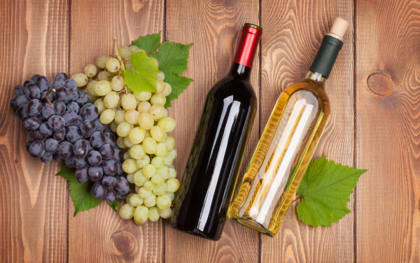 4K Ultra HD desktop wallpaper featuring two wine bottles, one red and one white, alongside bunches of red and white grapes on a wooden surface.