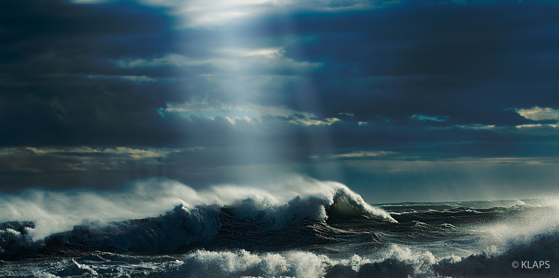 HD desktop wallpaper of ocean waves under a turquoise and blue sky, with clouds and sunbeams breaking through the horizon, showcasing nature's powerful beauty.