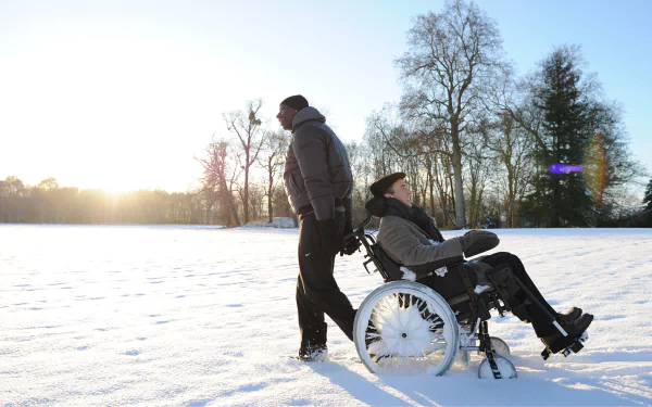 Sunrise over snow as a man pushes a smiling friend in a wheelchair, evoking a scene from the movie The Intouchables — HD desktop wallpaper.