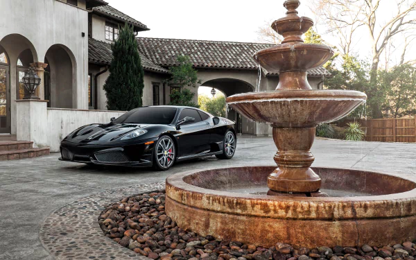 Black Ferrari F430 supercar parked beside a stone fountain in a cobblestone courtyard, HD PC desktop wallpaper background with Mediterranean villa and trees.