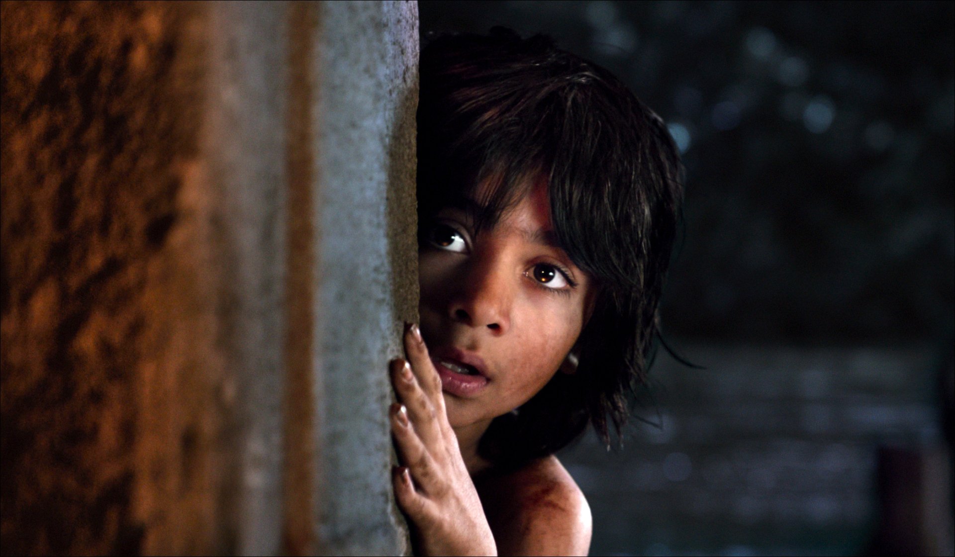 HD desktop wallpaper from the movie The Jungle Book (2016) showing Mowgli peeking cautiously from behind a tree trunk in a dark jungle setting.