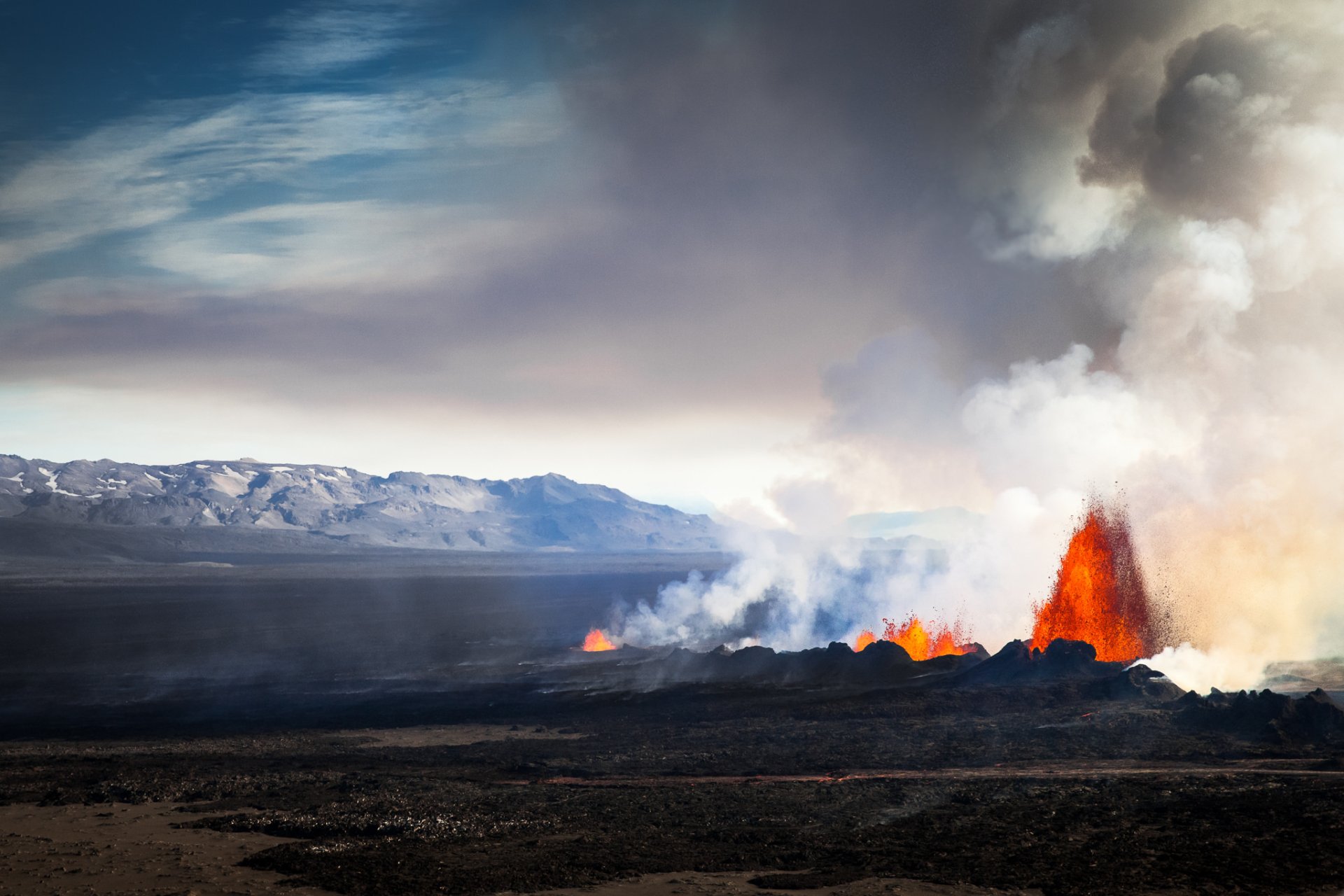 Bárðarbunga volcano eruption in Iceland with glowing lava and smoke rising over a dark volcanic landscape under a cloudy sky.