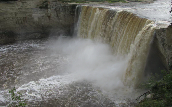 Alexandra Falls in Canada cascades powerfully into a river surrounded by rocky cliffs and lush greenery, captured in high-definition as a nature desktop wallpaper.