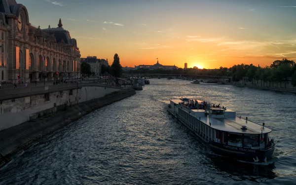 Passenger ship cruising the Seine river at sunset in Paris, France, captured in a 4K Ultra HD desktop wallpaper showcasing the evening sky and historic riverbanks.