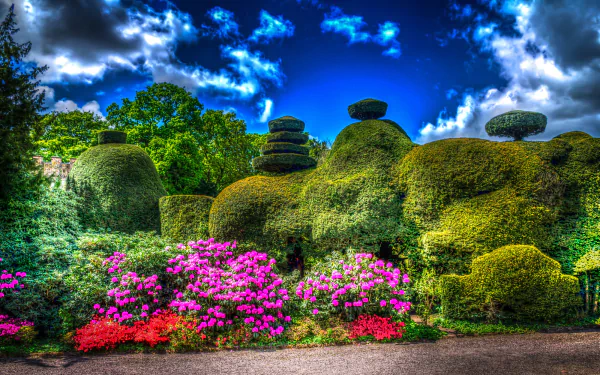Vibrant HDR photograph of an English garden in spring, featuring colorful flowers and sculpted trees under a dynamic blue sky, captured as an HD PC desktop wallpaper.