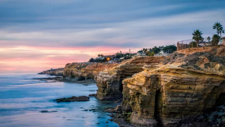HD PC desktop wallpaper: San Diego coastline at sunset — sandstone cliffs and coastal homes above a calm ocean under a pastel horizon, earth-and-sea photography