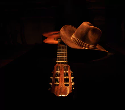 A still life composition featuring a guitar and a cowboy hat, captured in rich detail against a dark background. This HD image enhances desktop backgrounds with a musical theme.