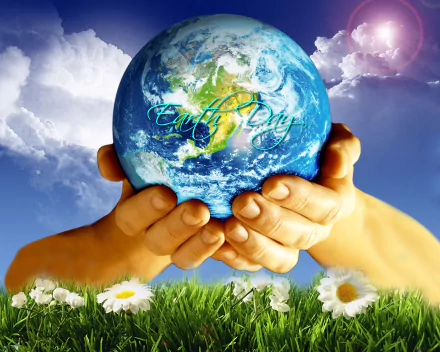 HD desktop wallpaper showing hands gently holding Earth with Earth Day text, set against a vibrant sky and grassy field with daisies, celebrating the holiday.