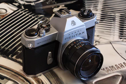 Close-up of a man-made vintage Pentax SLR camera on a reflective surface, 4K Ultra HD PC desktop wallpaper and background showing detailed lens, dials and chrome highlights.