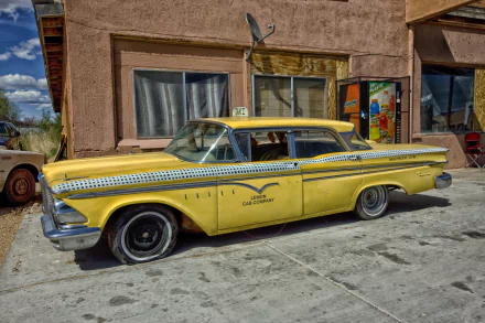 Vintage yellow 1950s Ford Edsel Ranger classic car taxi parked beside an old building under a blue sky, captured in HD for a desktop wallpaper background.