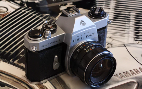 Close-up of a man-made vintage Pentax SLR camera on a reflective surface, 4K Ultra HD PC desktop wallpaper and background showing detailed lens, dials and chrome highlights.