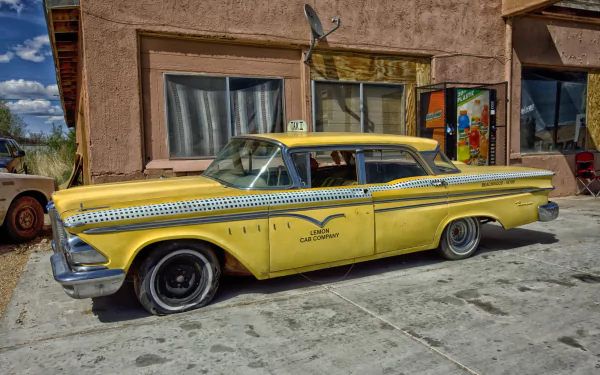 Vintage yellow 1950s Ford Edsel Ranger classic car taxi parked beside an old building under a blue sky, captured in HD for a desktop wallpaper background.