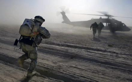 A soldier runs towards a Sikorsky UH-60 Black Hawk helicopter in a dusty landscape, capturing the intensity of military operations. HD wallpaper and background for PC use.