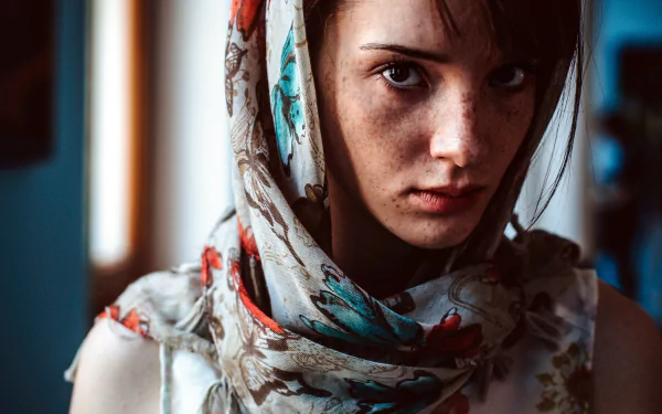 Close-up 4K Ultra HD wallpaper of a woman with brown eyes and freckles, wearing a patterned scarf, showcasing a captivating and natural face.