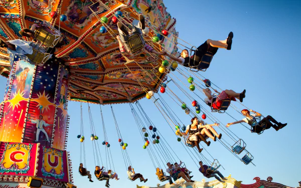 Vibrant carnival swing ride (man-made) at an amusement park, people on swinging chairs against a clear blue sky — HD PC desktop wallpaper/background.