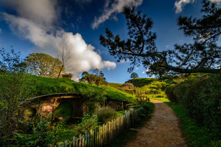 A vibrant HD desktop wallpaper showcasing the man-made Hobbiton set, featuring quaint hillside homes under a bright blue sky with fluffy clouds.