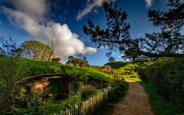 A vibrant HD desktop wallpaper showcasing the man-made Hobbiton set, featuring quaint hillside homes under a bright blue sky with fluffy clouds.