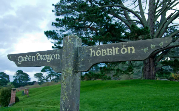 Man-made Hobbiton signpost reading Green Dragon and Hobbiton against lush rolling hills and trees — HD PC desktop wallpaper background.
