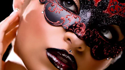 A close-up of a masked individual showcases deep red lips adorned with glossy lipstick and piercings, set against a dramatic dark background, creating an intriguing visual impact.